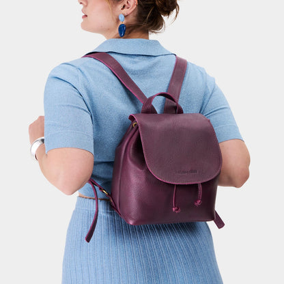 Plum | Pebbled purple leather drawstring backpack being worn by a person wearing a blue sweater.