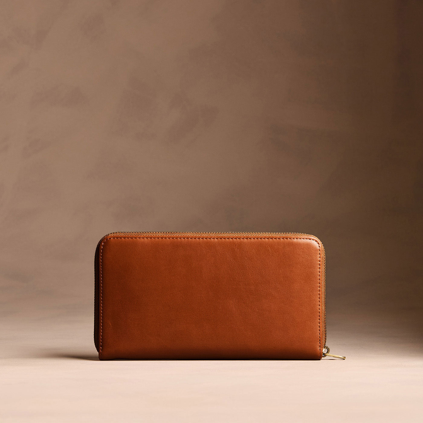 Vintage Tan | Full zip around wallet with a strap on a brown background