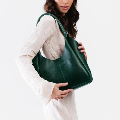 Forest Green*Large | A model holding a u-shaped, flat-bottomed leather shoulder bag with two outside pockets