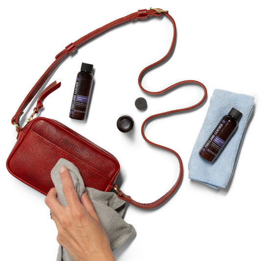 2oz | A hand applying rain and snow shield to a purse with a micro-fiber cloth